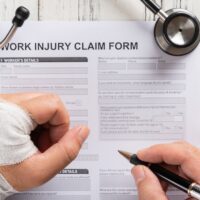 top view man filling up a work injury claim form with stethoscope  medical and insurance concept