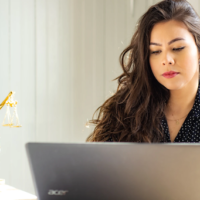 Woman using laptop on table with sculpture of Lady Justice.