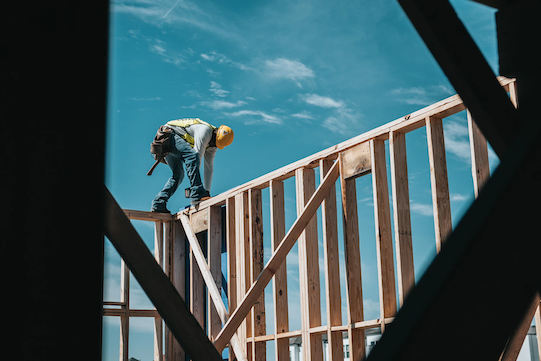 Construction worker precariously working on house frame.