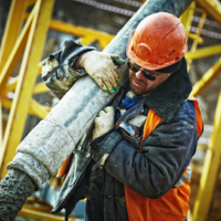 Construction worker carries pipe at worksite