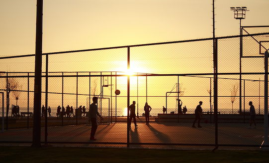 People playing basketball in a public park at sunset.