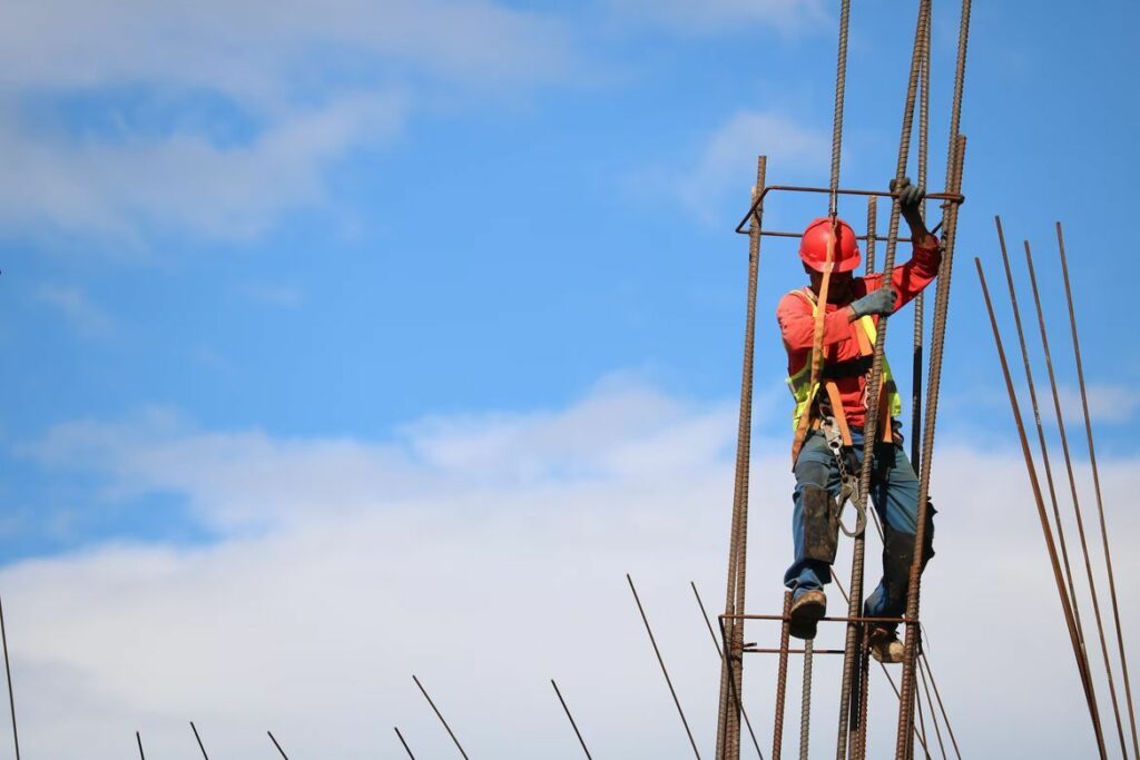 A construction worker securing metal poles high above the ground.