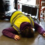 Accident in the work place, young woman lies injured after falling from step ladder onto the factory floor
