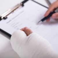 High Angle View Of A Person With Fractured Hand Filling claims form