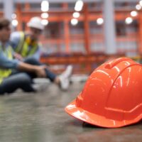 Close Up on Red Hard Hat with Blurred Injured Factory Workers as a Background