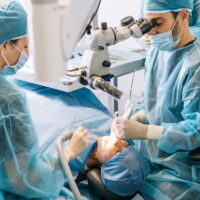 doctor operating man in cabinet with eyes closed during procedure made by dentist and assistant.