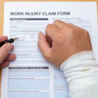 filling up a work injury claim form with a wrapped hand medical and insurance concept