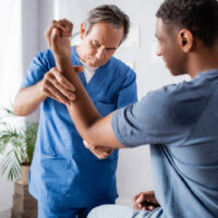 chiropractor working with injured arm of african american man in clinic chiropractor working with injured arm of african american man in clinic