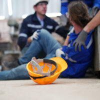 Worker receiving industrial injury in factory and colleague helping him while injured on leg.