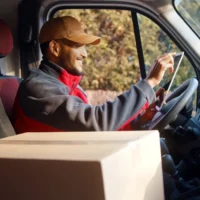 a-delivery-driver-in-a-red-jacket-and-cap-smiles-while-using-a-digital-tablet-inside-a-van a-delivery-driver-in-a-red-jacket-and-cap-smiles-while-using-a-digital-tablet-inside-a-van